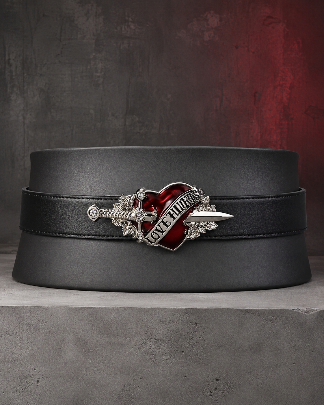Love Hurts black belt with red heart and silver dagger buckle displayed on a concrete block